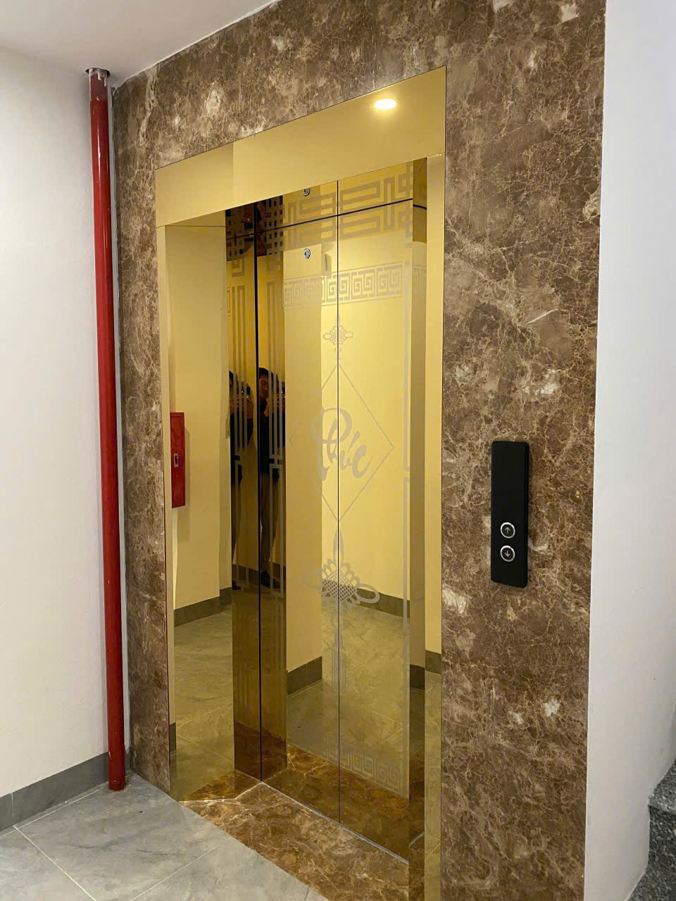 Thang máy cửa kính màu vàng viền đá marble nâu trong sảnh tòa nhà hiện đại